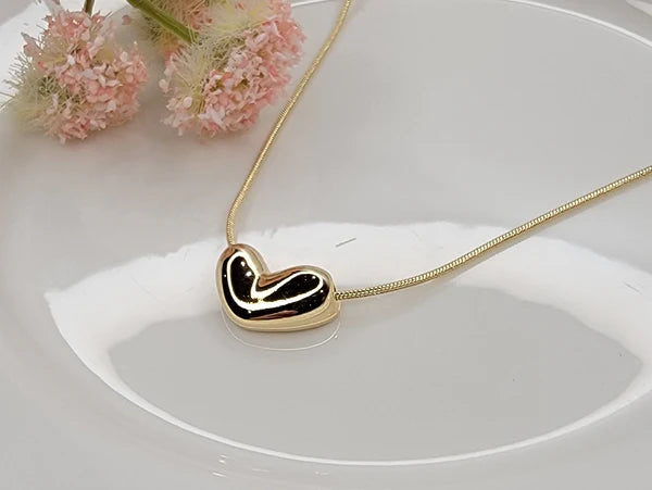 Gold necklace with an irregular heart-shaped pendant on a white dish with pink flowers in the background