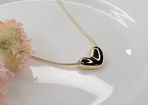Gold necklace with an irregular heart-shaped pendant on a white surface with pink flowers.