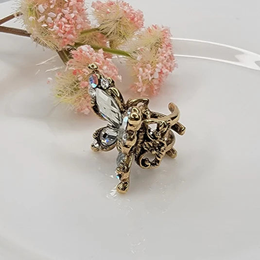 Gold butterfly design hair clip on a white surface with pink flowers in the background