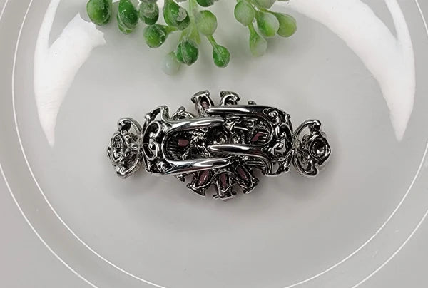 Back of a silver hair clip with gemstones on a white plate with greenery