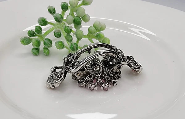 Side view of a silver hair clip with intricate design on a white plate with green decorative elements