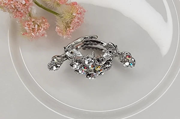 Side view of silver hair clip with gemstones on a white surface with pink flowers.